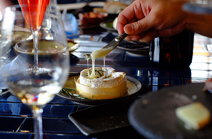 A baked wheel of camembert with honey and rosemary on top with a knife cutting into it and the melted cheese dripping down